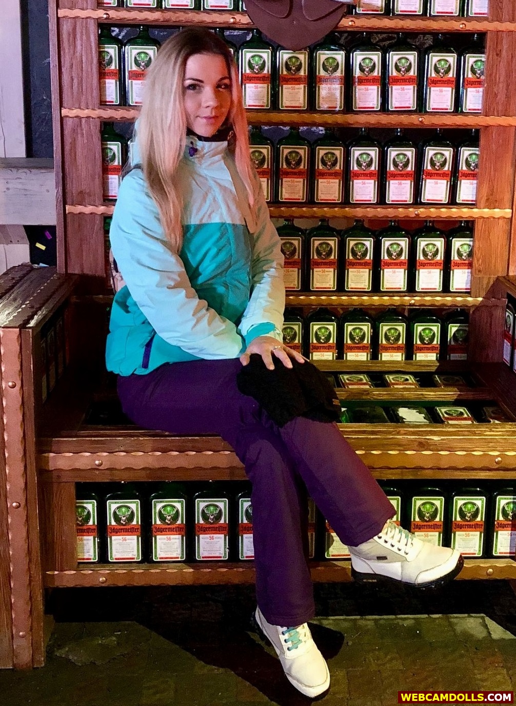 Blonde Girl sitting in Purple Ski Suit and Green Anorak on Webcamdolls